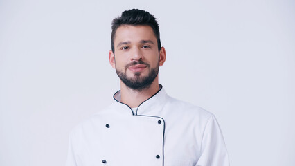 positive bearded chef in uniform looking at camera isolated on white.