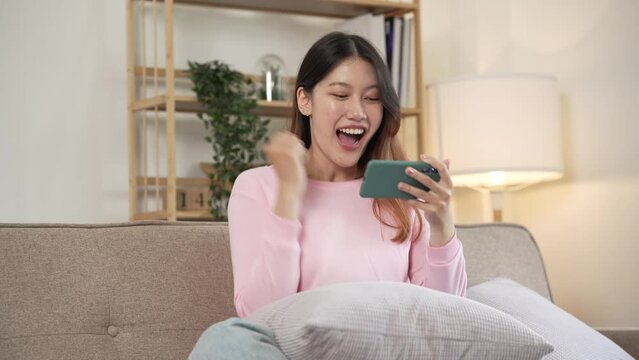 Young asian woman playing mobile games on sofa.