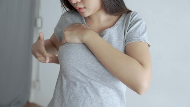 Asian woman wearing a gray T-shirt is self-checking for breast cancer.