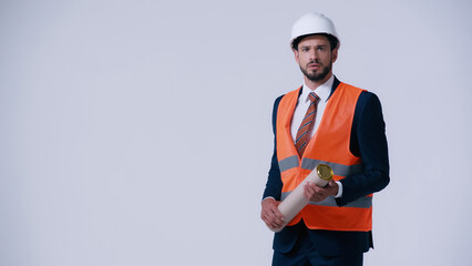 worried architect in safety vest and hardhat holding blueprint tube isolated on grey.