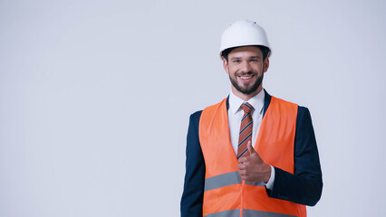 happy foreman in safety vest and helmet showing thumb up isolated on grey.