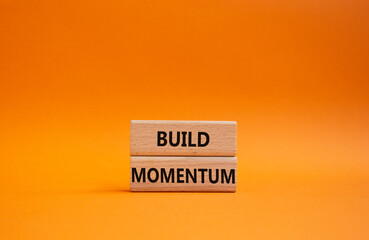 Build momentum symbol. Wooden blocks with words Build momentum. Beautiful orange background....
