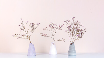 Three bouquet of dried flowers in a plaster vases on a table against the pale pink wall, front view. Home decor.