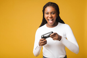 African american gamer woman playing video game using joystick over isolated yellow background. Very happy female looking to the camera © Vadim Pastuh