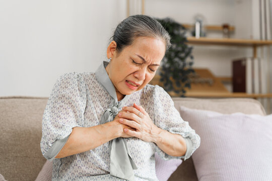 Senior asian mature woman heart disease, sitting on couch.