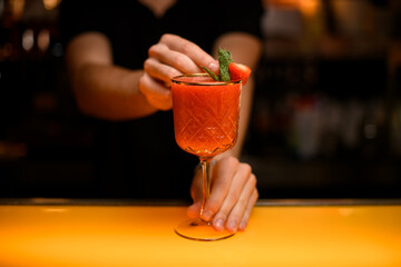 close-up of goblet with signature cocktail which hand of bartender decorate with mint leaf and strawberry © fesenko