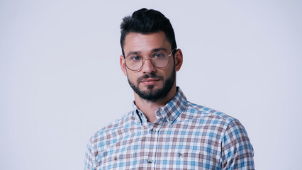 young bearded nerd in eyeglasses and plaid shirt looking at camera isolated on grey.