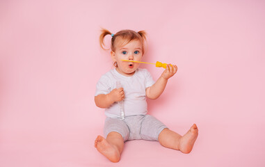 Portrait of a surprised cute little baby girl on a pink background. A child model blows soap bubbles and has fun. Advertising of children's goods