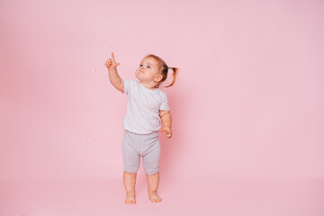 Cute little happy girl standing, looking and pointing up on a pink background, Advertising of...