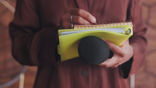 Microphone and notepad in hands woman journalist interviewing interesting person and writing down words of interlocutor in notebook for further sending to editor or publishing post on own blog