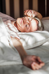 Happy middle aged woman sits on bed and stretching arms