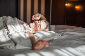 Happy middle aged woman sits on bed and stretching arms