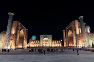 People on the Registan Square in the late evening admire the multi-colored illumination of the...