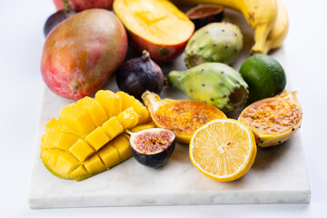 A fresh tropical exotic fruit plate on marble board: mango, pitaya, lemon, lime, banana, fig