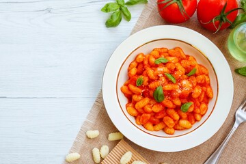 Italian Traditional Dish"Gnocchi al Pomodoro"potato gnocchi with tomatoes,olive oil,garlics,parmesan,salt and basil on plate with white wood background.Easy and healthy vegetarian pasta.Top view