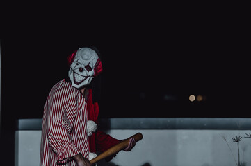 Asian handsome man wear clown mask with weapon at the night scene,Halloween festival concept,Horror scary photo of a killer in orange cloth,Evil clown charactor