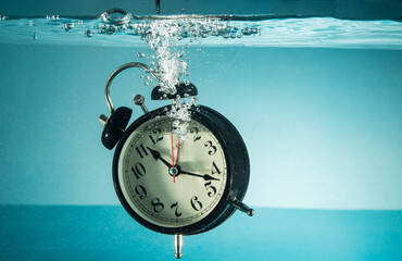 Table clock sinking into blue water tank - concept of time management with copy space