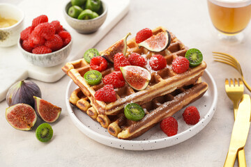 Fresh homemade sweet belgian waffles with honey, powdered sugar with fresh raspberries, kiwi berries and figs on white plate