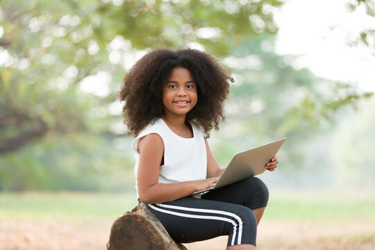 Happy African American child girl using laptop computer outdoors in the park. Kid girl learning outside at the school