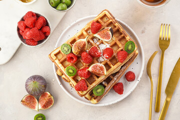 Fresh homemade sweet belgian waffles with honey, powdered sugar with fresh raspberries, kiwi berries and figs on white plate, top view