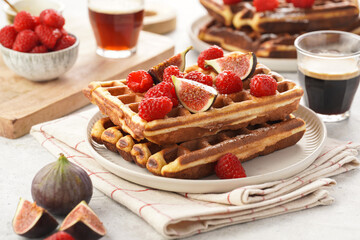 Fresh homemade sweet belgian waffles with honey, powdered sugar with fresh raspberries, kiwi berries and figs on white plate
