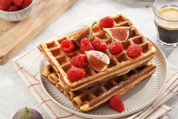 Fresh homemade sweet belgian waffles with honey, powdered sugar with fresh raspberries, kiwi berries and figs on white plate