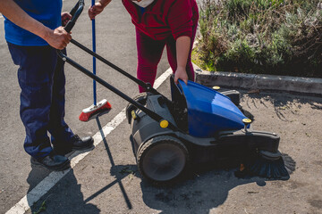 Obraz premium Two young latino janitorial workers (man and woman) in uniform cleaning in parking lot with outdoor industrial vacuum cleaner