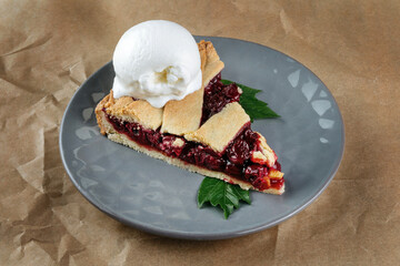 Homemade cherry cobbler pie with flaky crust, ice cream. 45 view, the plate is on craft paper.