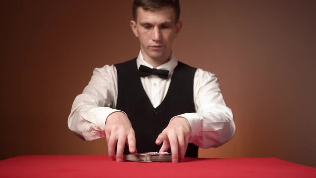 Young caucasian casino dealer puts cards on the red table, close-up hands.