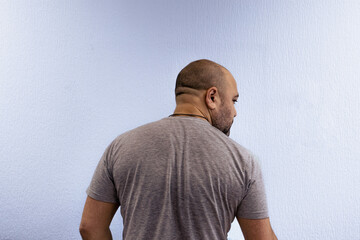 A man stands with his back against a white wall. Back of a bald man with a short haircut