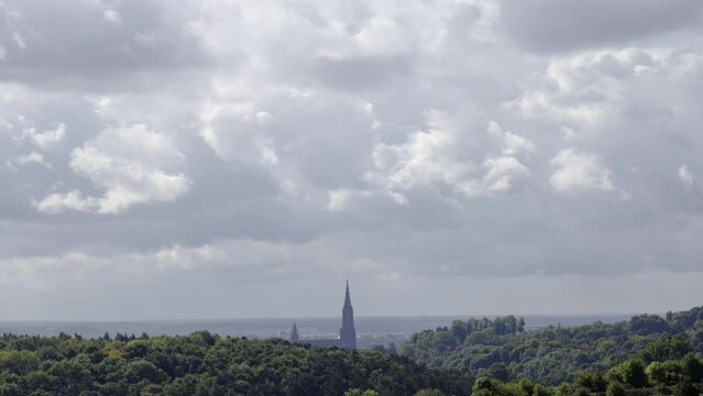 Time lapse shot of Ulm minster behind a forest with heavy clouds passing. Some sun rays brake through the clouds.