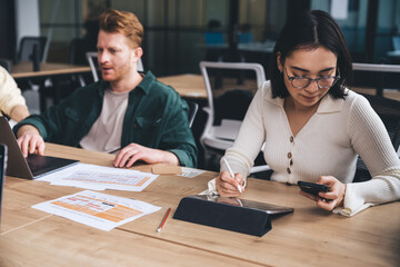 Diverse colleagues sitting at desk and working on gadgets at workplace