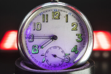 An old pocket watch with dangerous radioactive fluorescent paint. Scratches on the glass. Silver chrome metal. Black background. Violet light and green glow of numbers.