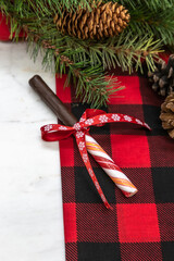 Chocolate dipped candy cane, red checkered kitchen towel, pine cones, ribbon, pine needles, pine branch, marble cutting board, Christmas concept, perspective view.