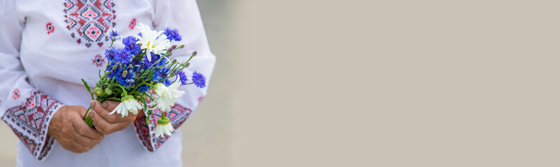 An old Ukrainian woman in an embroidered shirt with a bouquet of flowers. Selective focus.