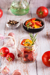 Homemade sun-dried tomatoes with spices, garlic and herbs in a jar and fresh vegetables. Vertical