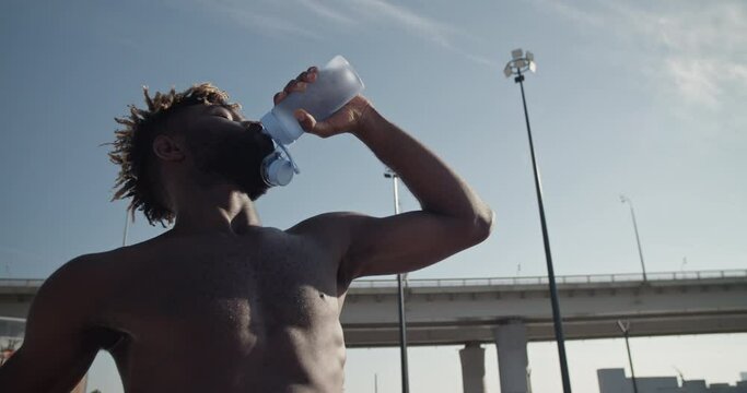 Black sportsman drinking water against blue sky