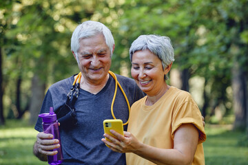 Attractive elderly spouses using modern smartphone after sportive work out