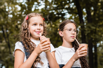 Two pupils are drinking from eco-friendly cups and straws a drink in the park on a warm day