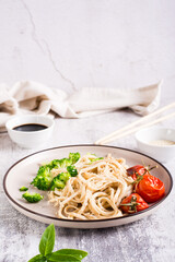 Wheat udon noodles in soy sauce with tomatoes and broccoli on a plate on the table. Vertical view