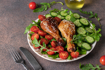 Baked chicken drumsticks with cherry tomato, cucumber and arugula salad on brown background, Copy space