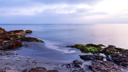 Fototapeta na wymiar Cloudy sunrise on a beach with sand and rocks