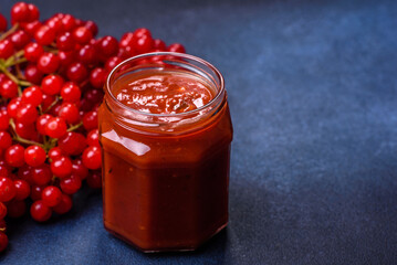 Viburnum fruit jam in a glass jar on a dark concrete background