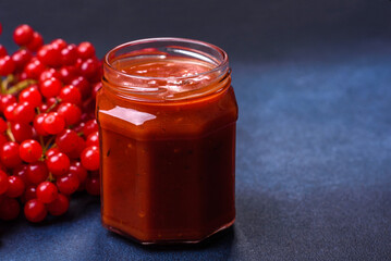 Viburnum fruit jam in a glass jar on a dark concrete background