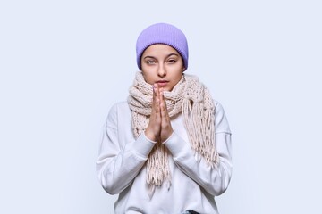 Winter portrait of young female in sweater hat scarf, on light studio background