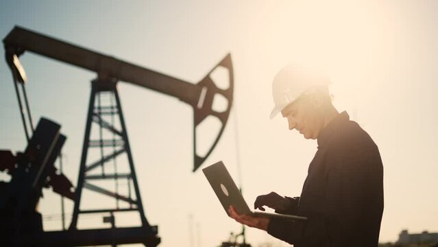 oil industry. engineer next to an oil rig. oil business production finance concept. gas production. a worker with sun a laptop monitors oil production next to an station. a worker in hard hat works