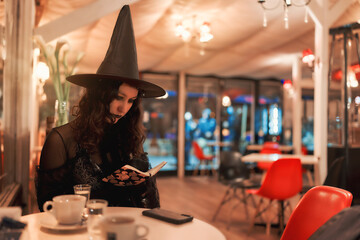 young latin woman dressed as a witch sitting and reading a book in a cafe
