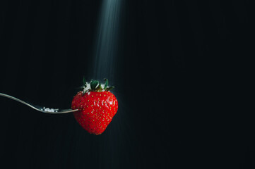 fresh ripe red strawberries impaled on a silver fork and sugar falling on it. black background....