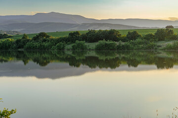 Reflection of bushes and mountains on the bank of a dam