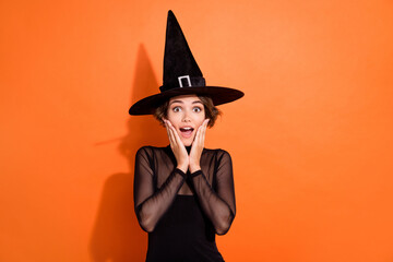 Photo of excited funky girl dressed black gothic dress headwear hands arms cheeks cheekbones empty space isolated orange color background